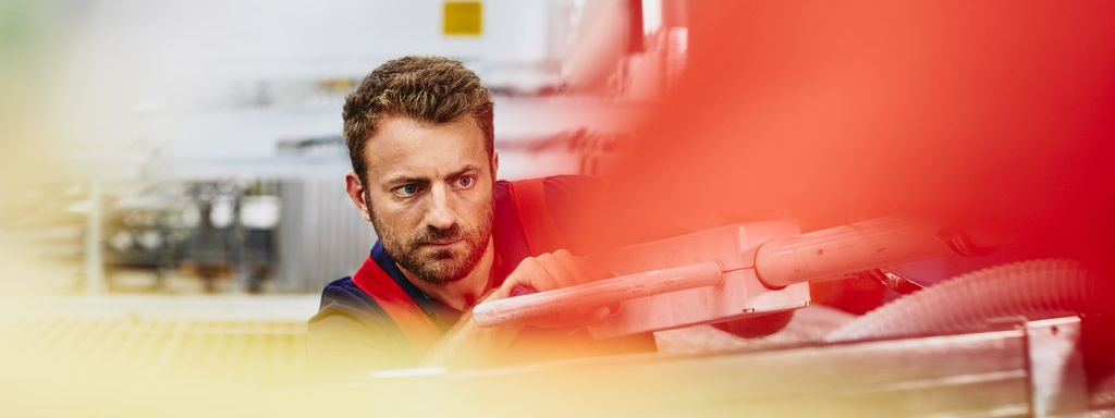 Blue-collar worker aligning something. Primary color red.